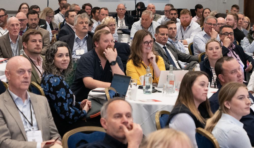 Conference audience sat at tables facing speakers.